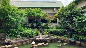 A courtyard with a stone water feature, lush greenery, and a building with a green roof. - Palace Hotel KAKEGAWA (Kakegawa)