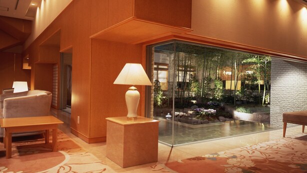 A modern lobby with a glass wall, wooden furniture, and a small indoor garden. - Palace Hotel KAKEGAWA (Kakegawa)