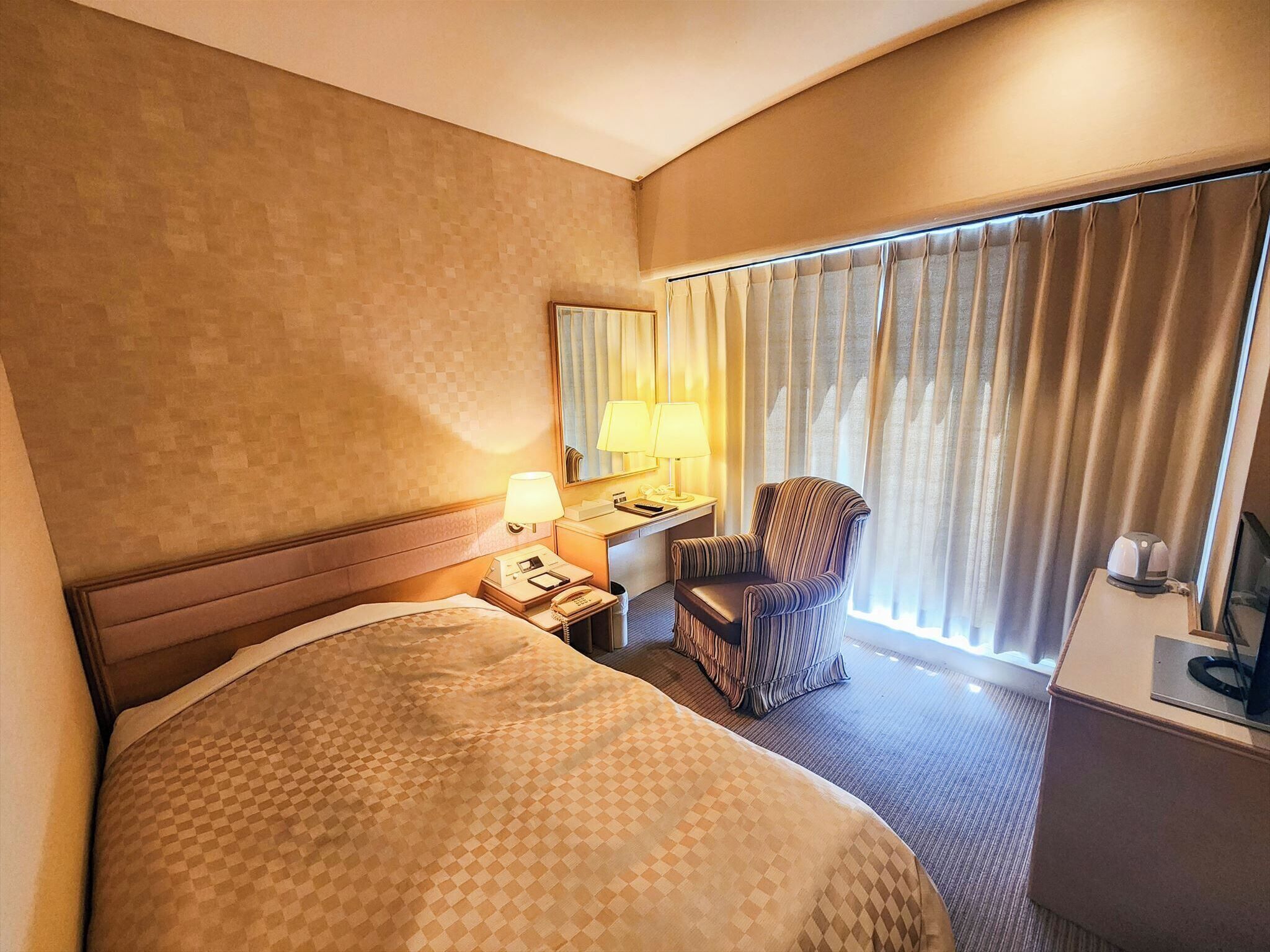 Une chambre d’hôtel avec un grand lit, un bureau avec une lampe, une chaise et un téléviseur posé sur un meuble.