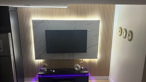 Ein modernes Wohnzimmer mit einem an der Wand mit Marmoroptik befestigten Flachbildfernseher, einer dunklen Unterhaltungsecke mit Globus und Vase sowie einem Sofa mit passendem Hocker.