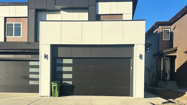 Ein modernes, zweistöckiges Haus mit Garage, Auffahrt und einer kleinen, grünen Mülltonne.