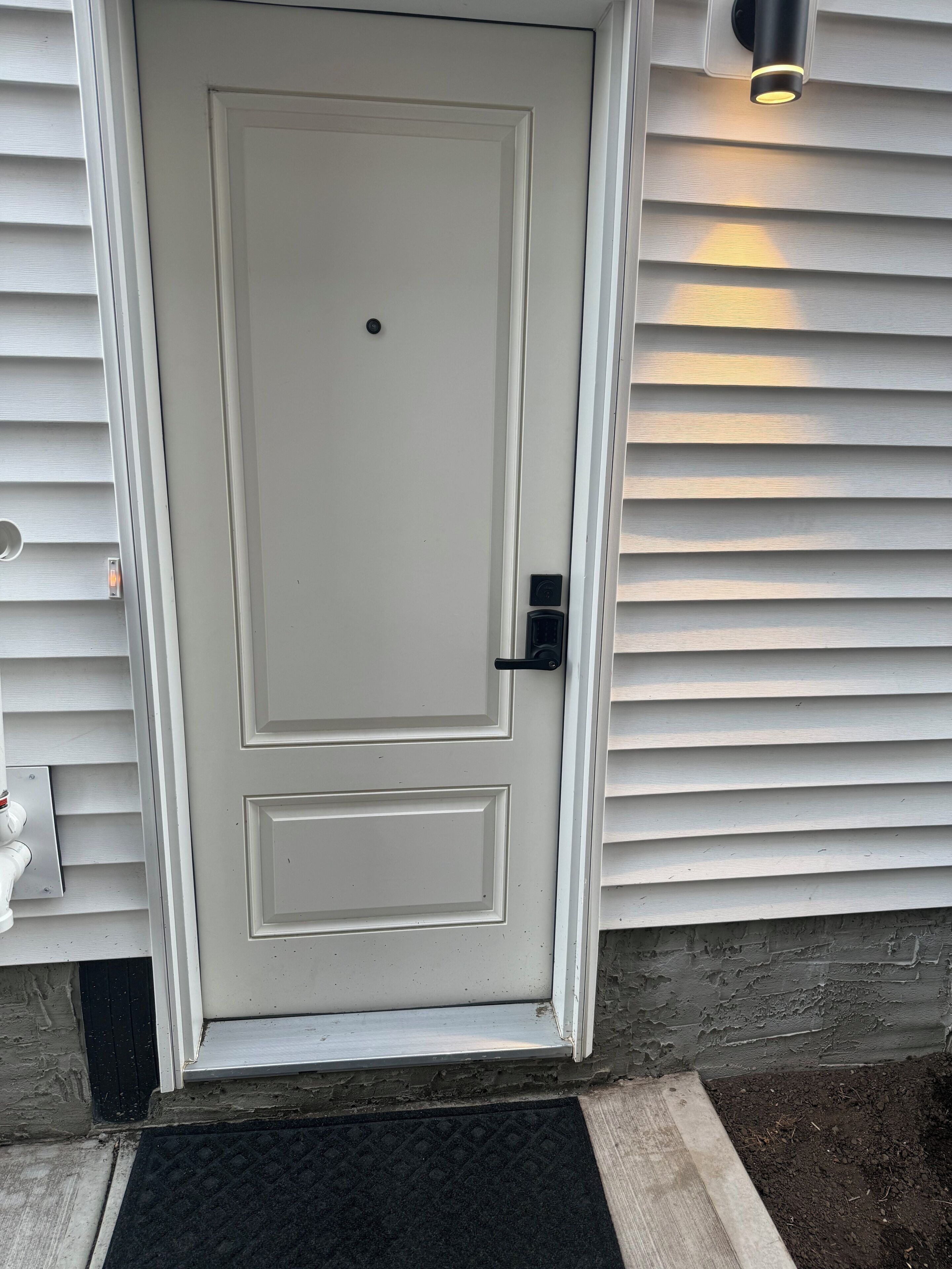 Puerta blanca con un pequeño panel rectangular, un picaporte negro y una lámpara encima.
