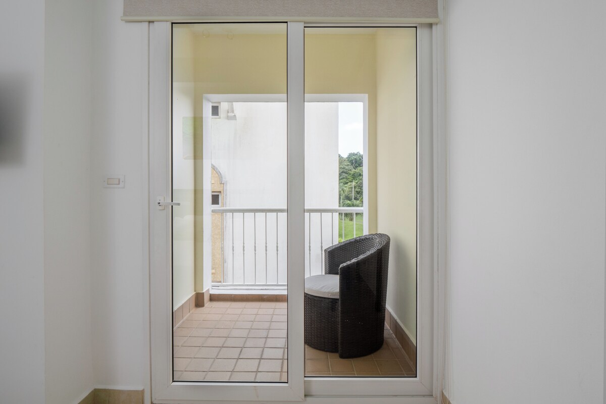 A room with a sliding glass door leading to a balcony with a wicker chair and a small table.