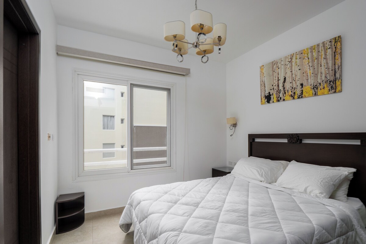 A bedroom with a bed, a window, a painting, and a chandelier.