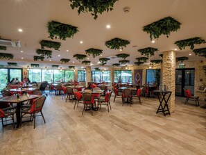 A spacious restaurant with wooden flooring, red cushioned chairs, and hanging green plants. - Mahogany Suites (Rousseau)