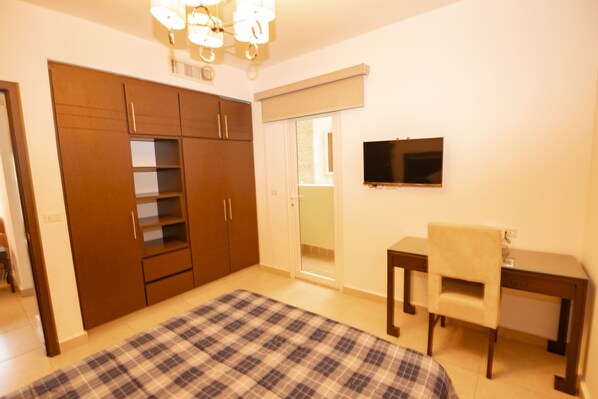 A bedroom with a bed, a desk, a chair, a television, and a wardrobe. - Mahogany Suites (Rousseau)