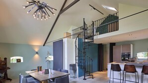 Una cocina moderna con una isla central, un comedor con mesa y sillas de madera, y una escalera de caracol que sube a un nivel superior.