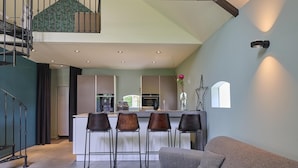 Una cocina moderna con una isla central, taburetes de bar y una escalera que sube a un nivel superior.