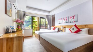 Quarto de hotel com duas camas, uma escrivaninha e uma janela grande com vista para o verde.