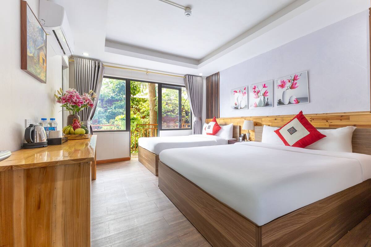 A hotel room with two beds, a desk, and a large window with a view of greenery.