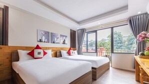 Quarto de hotel com duas camas, cabeceiras de madeira, uma mesa de madeira e uma grande janela com vista para áreas verdes.
