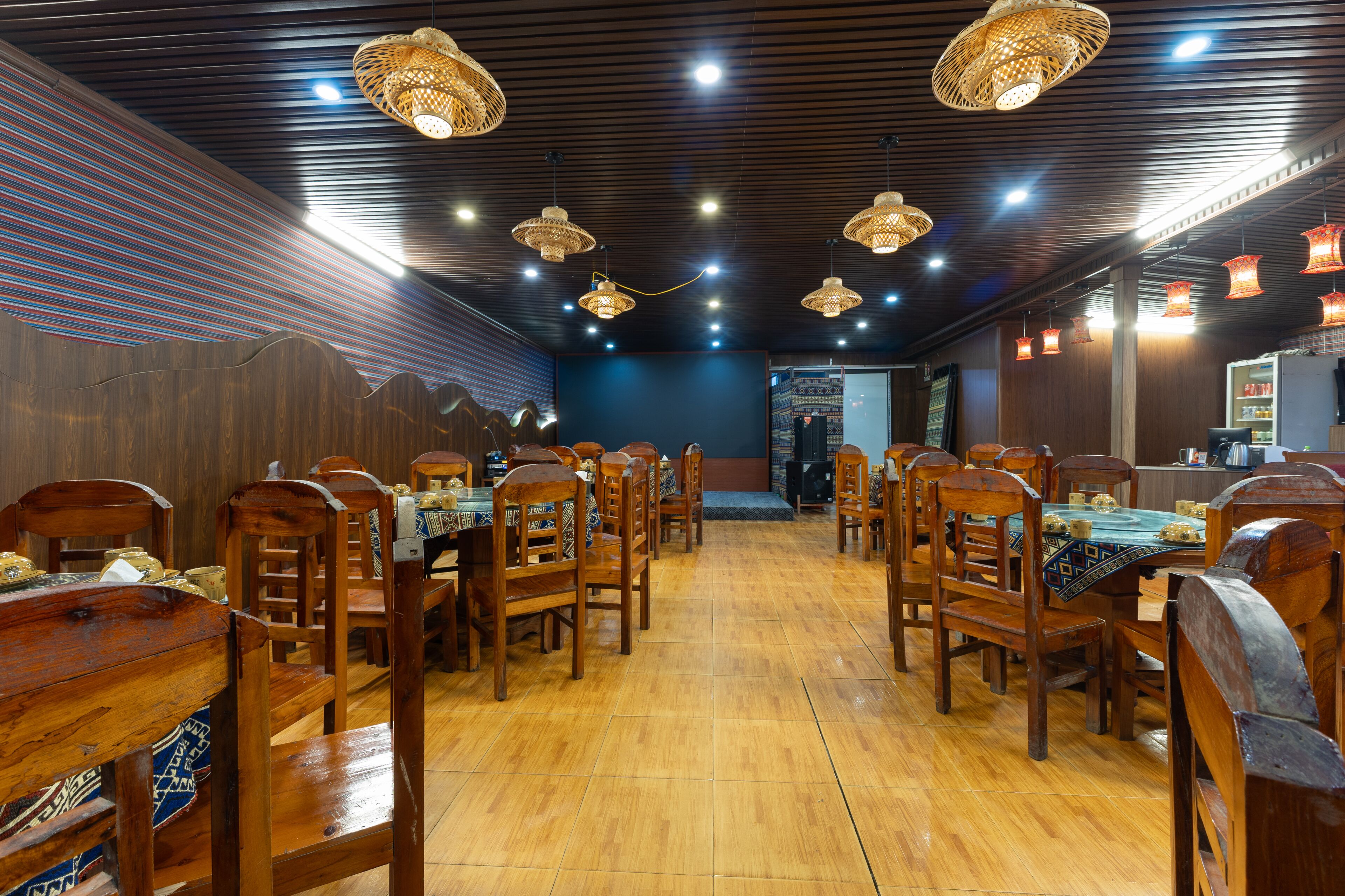 A restaurant with wooden tables and chairs, a blue wall, and hanging wicker lamps.