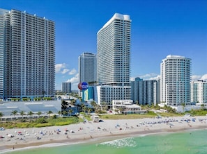 Um hotel à beira-mar com edifícios altos, uma praia de areia e um céu azul límpido.