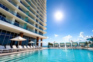 A hotel pool area with multiple levels of balconies, sun loungers, and umbrellas.