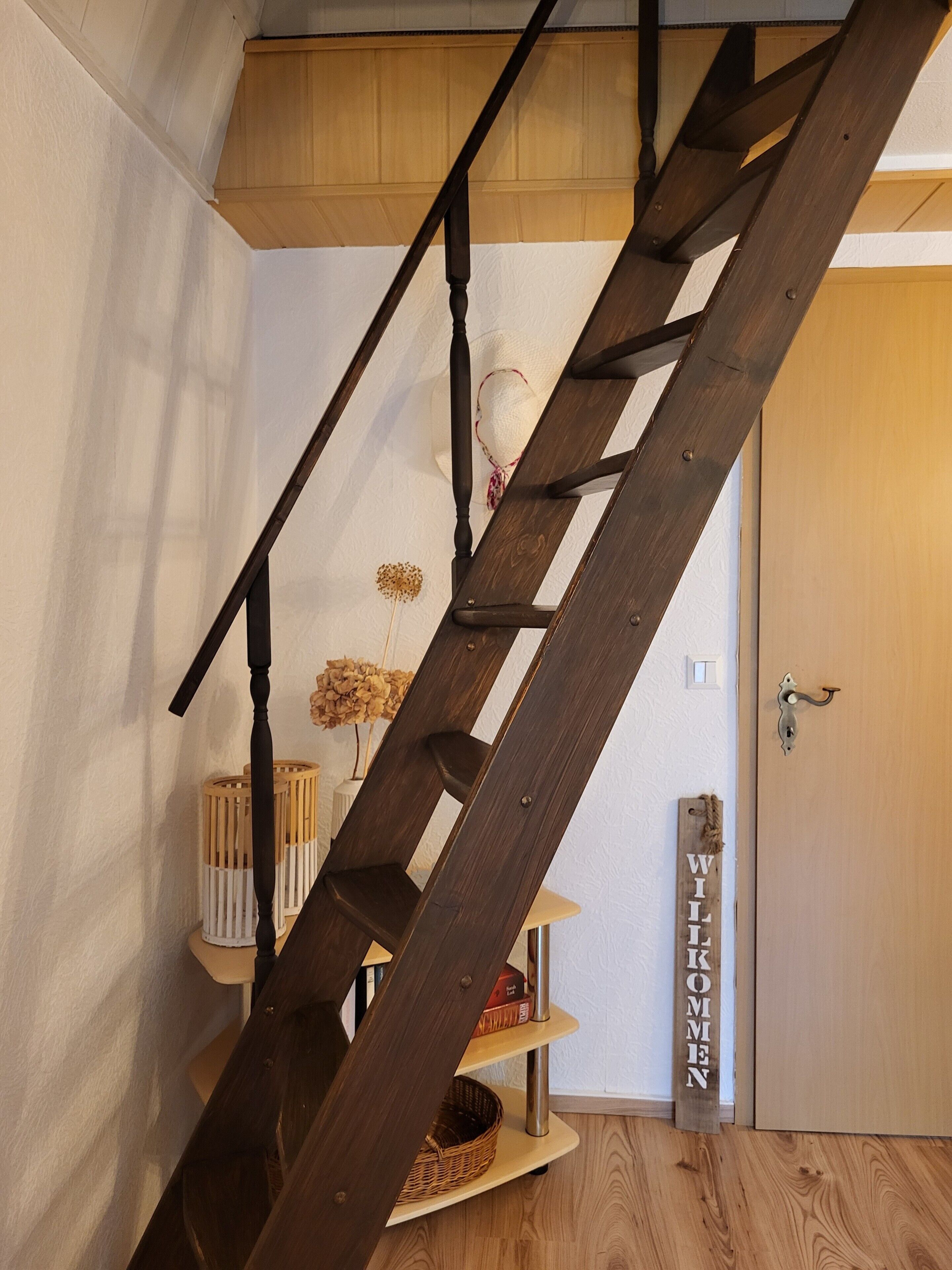A wooden spiral staircase with a white wall and a door with a metal handle.