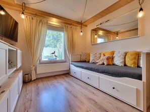 A room with a bed, a window with curtains, a radiator, and a shelf with a TV.