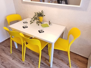 A dining table with four yellow chairs, a potted plant, two glasses, and a notebook.