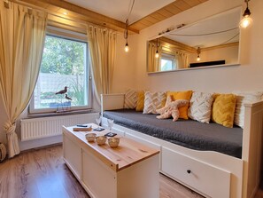A bedroom with a bed, bedside table, window with curtains, radiator, and a bird outside.