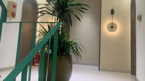 Interior moderno com escada, uma planta grande em vaso e luminária fixada na parede.