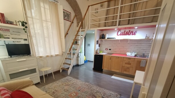 A modern living room with a sofa, a TV, and a staircase leading to a kitchen area. - Small apartment in the center of Rome (Roma)
