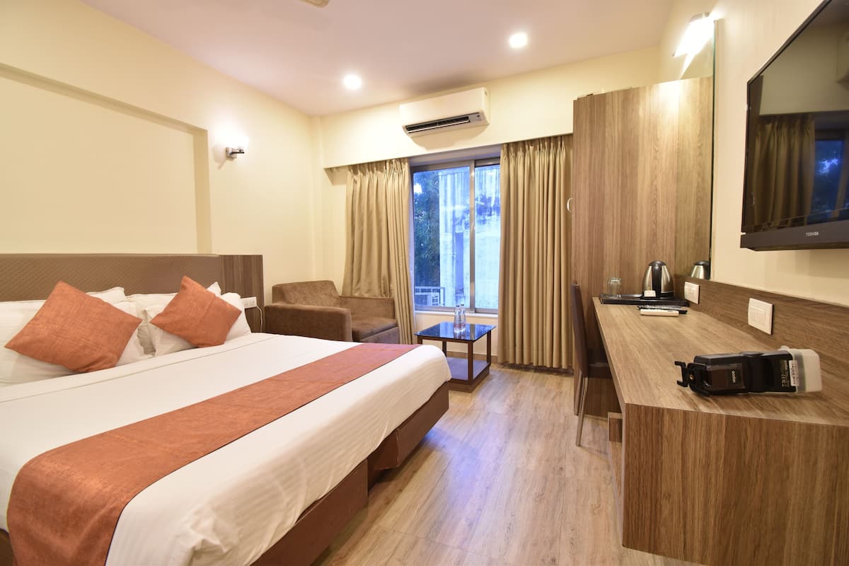 A hotel room with a large bed, a desk, a chair, and a TV.