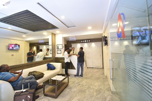 Zona de recepción con mostrador, área de espera con sofá y mesa de centro, y un televisor montado en la pared.
