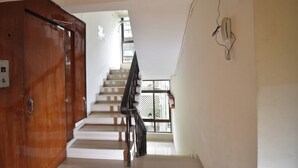 A staircase leading to a landing with a wooden door and a wall-mounted telephone. - Hotel Atlantic (Mumbai)