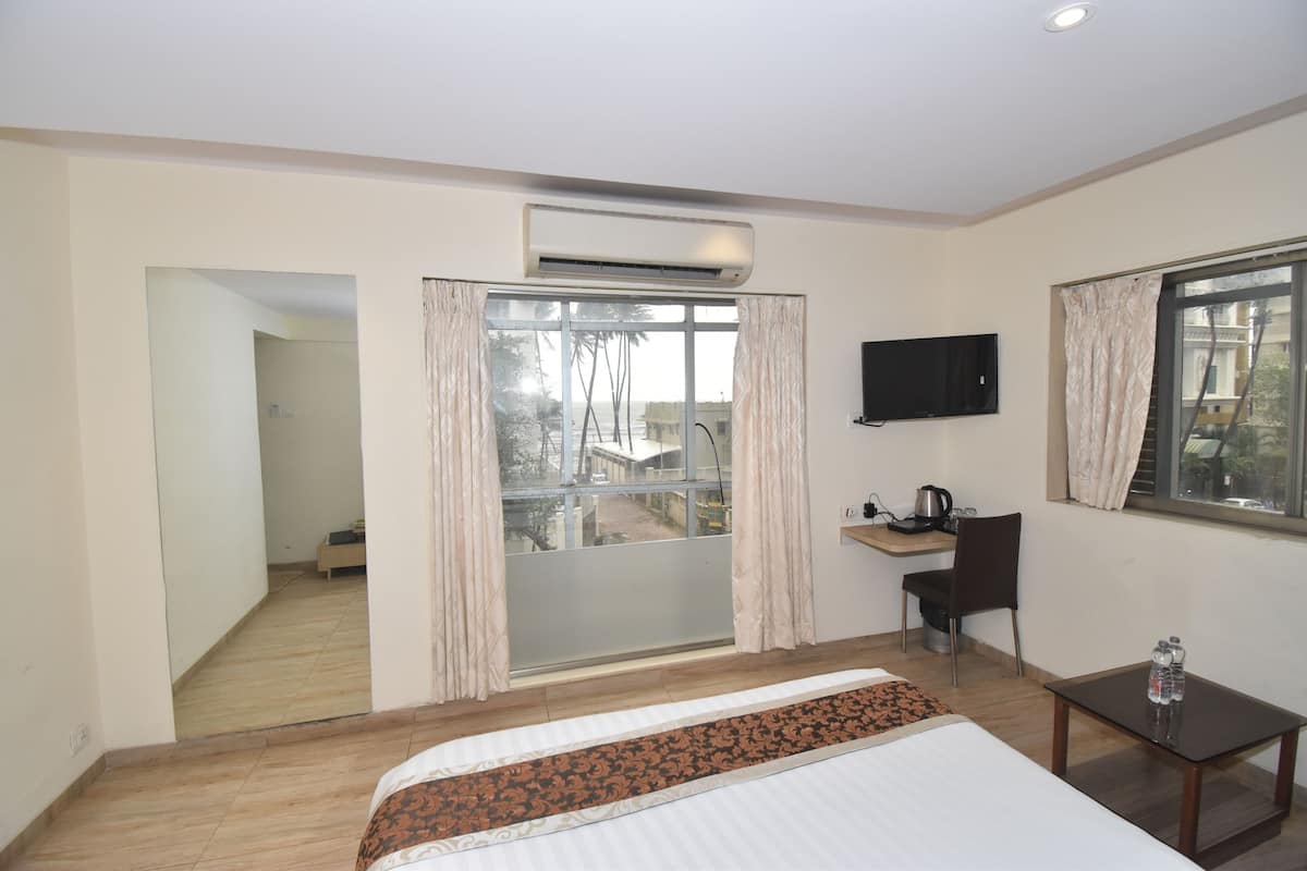 A hotel room with a bed, a desk, a chair, a TV, and a window with curtains.