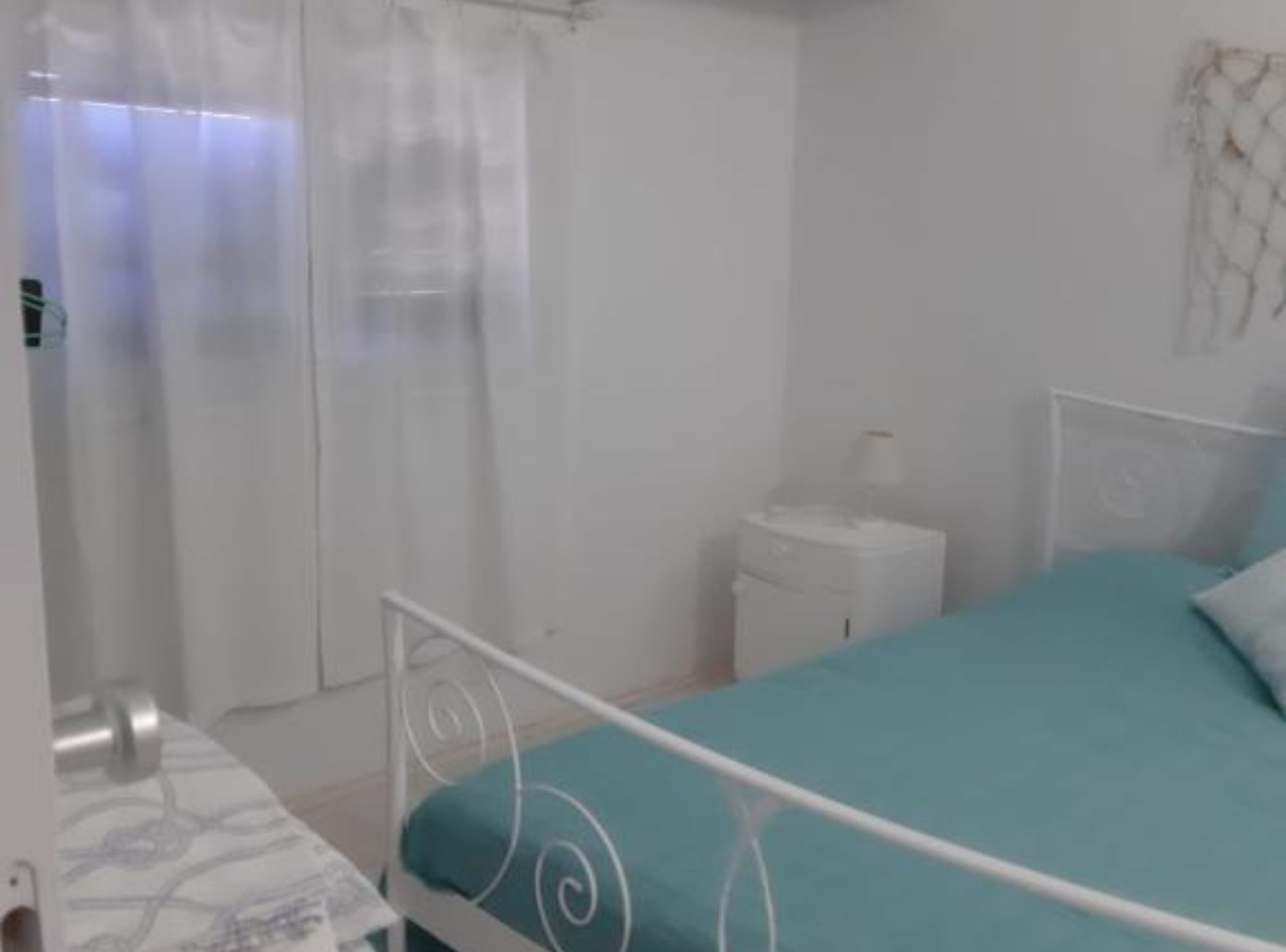 A bedroom with a bed, a bedside table, a nightstand, and a curtain.