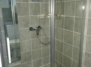 Et bruseområde med glasdør, flisebeklædte vægge og et håndholdt brusehoved.