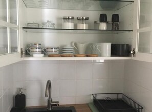 Et køkken med hvide fliserede vægge, en rustfri stålvask og hylder med køkkenudstyr.