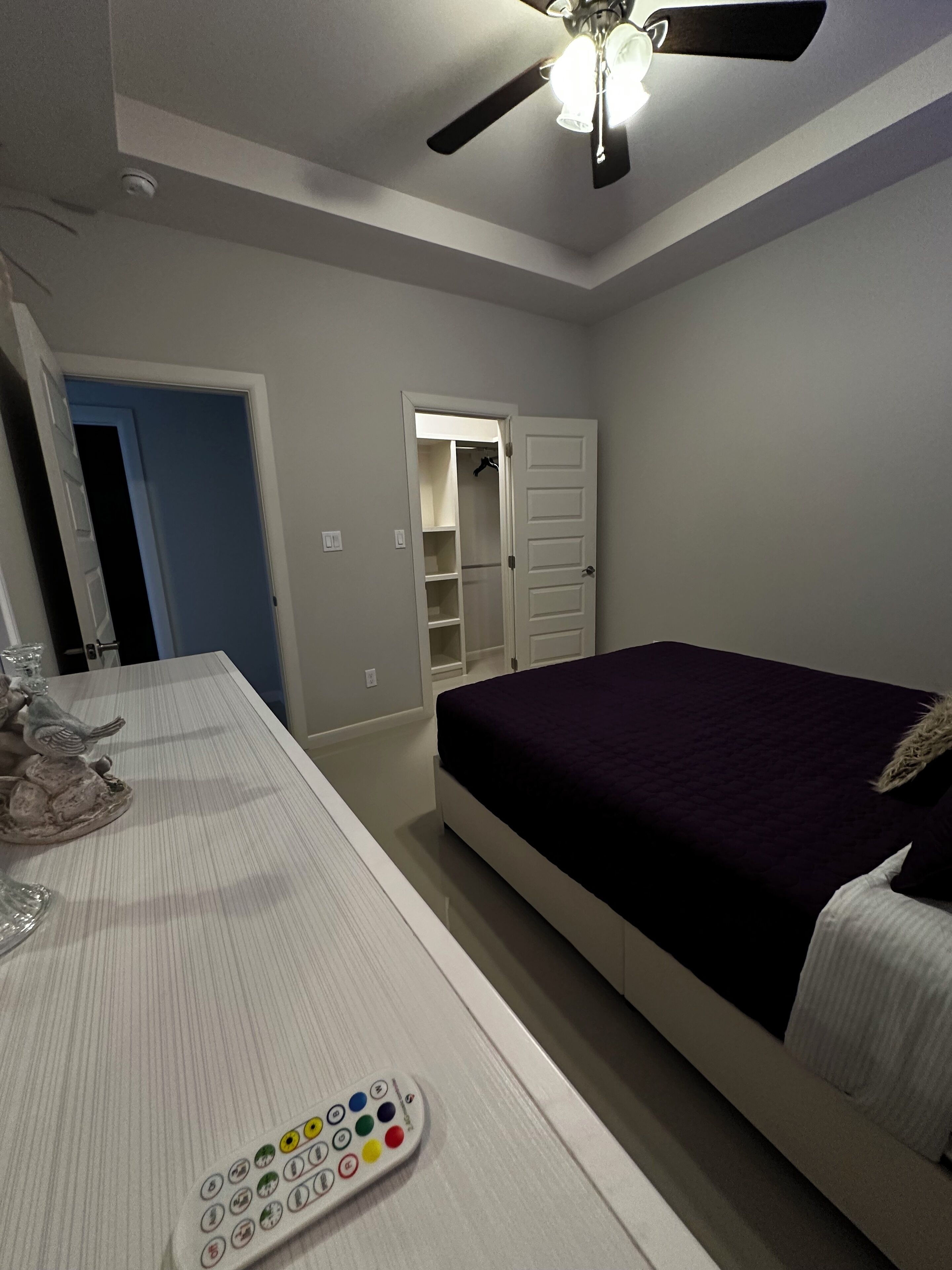 A bedroom with a bed, a ceiling fan, a nightstand, and a remote control.