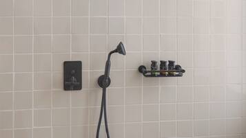 A shower area with a handheld showerhead, a wall-mounted control panel, and a soap dish.