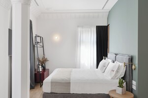 Egy modern hálószoba, amelyben található egy ágy, egy éjjeliszemélyzet, egy lámpa és egy függönnyel ellátott ablak.