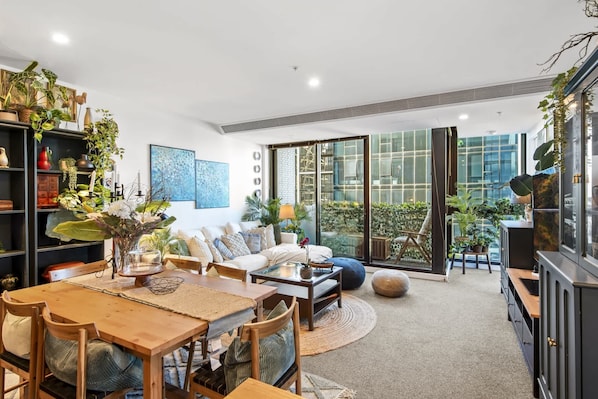 Un salon moderne avec un coin repas, de grandes fenêtres et des plantes d’intérieur.