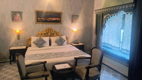 A traditional room with a large bed, two nightstands, a chair, and a window with curtains. - janak vilas (Udaipur)