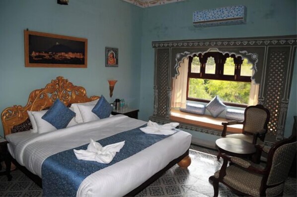 A bedroom with a bed, a window with a view, a chair, and a decorative wall. - janak vilas (Udaipur)