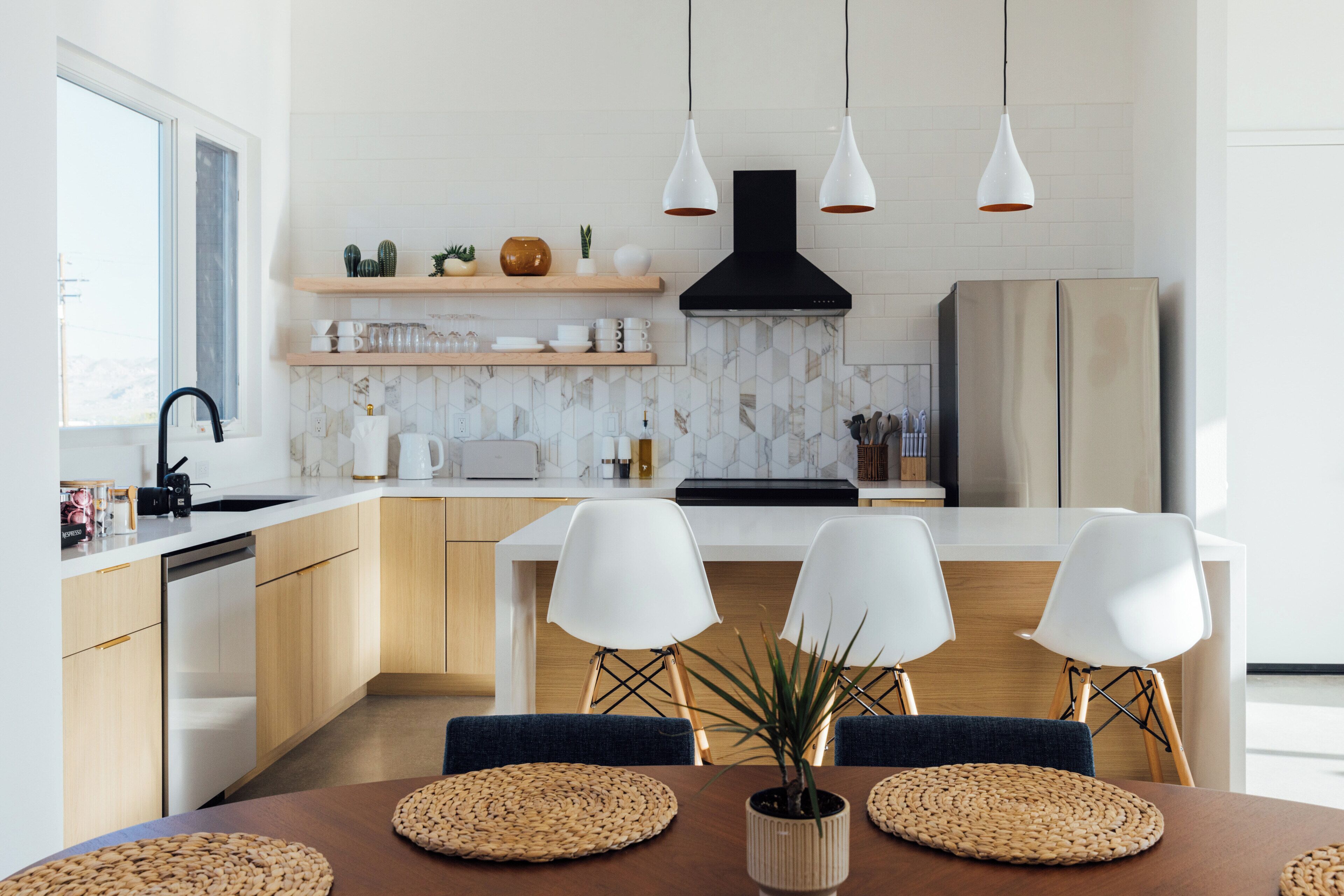 A modern kitchen with white cabinets, a black range hood, and a wooden dining table with four chairs.