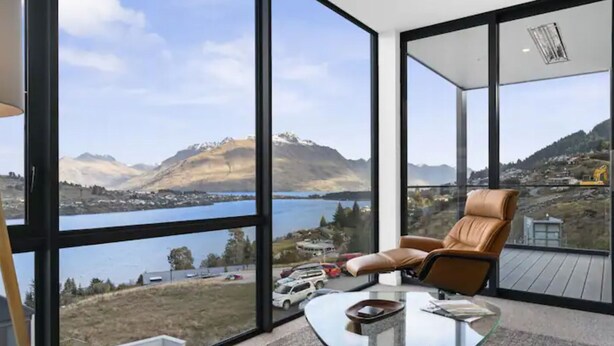 Ein modernes Zimmer mit großen Fenstern und Blick auf einen See und Berge.