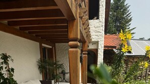 A covered outdoor seating area with a wooden pergola, potted plants, and a tiled floor.
