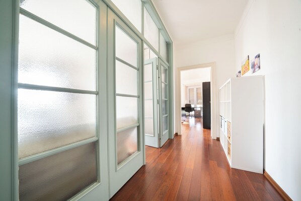 A hallway with wooden flooring, frosted glass doors, and a white refrigerator.