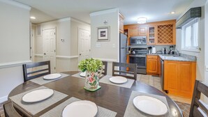 A dining area with a wooden table set for four, a kitchen with wooden cabinets and stainless steel appliances, and a small island with a sink. - Resort Condo w/ Marina Access in Williamsburg! (Williamsburg)