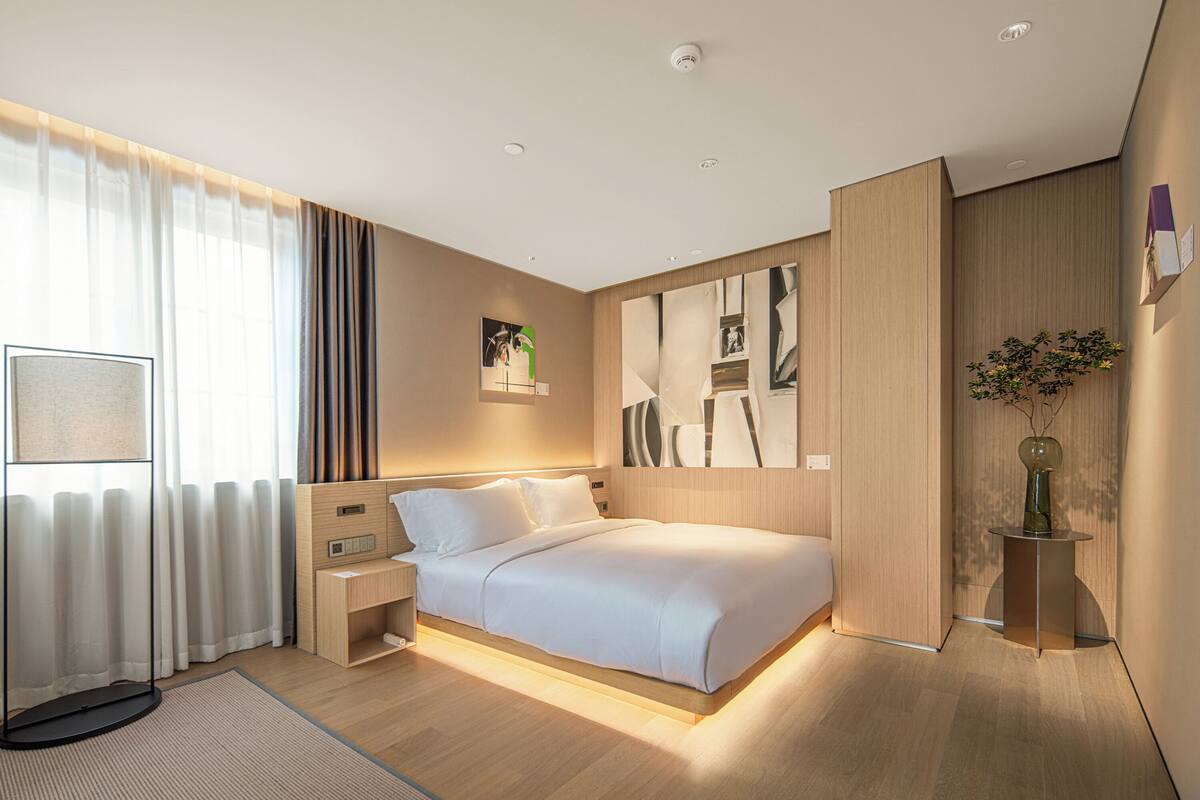 Une chambre d’hôtel moderne avec un grand lit, des tables de chevet, un bureau et une fenêtre avec des rideaux.