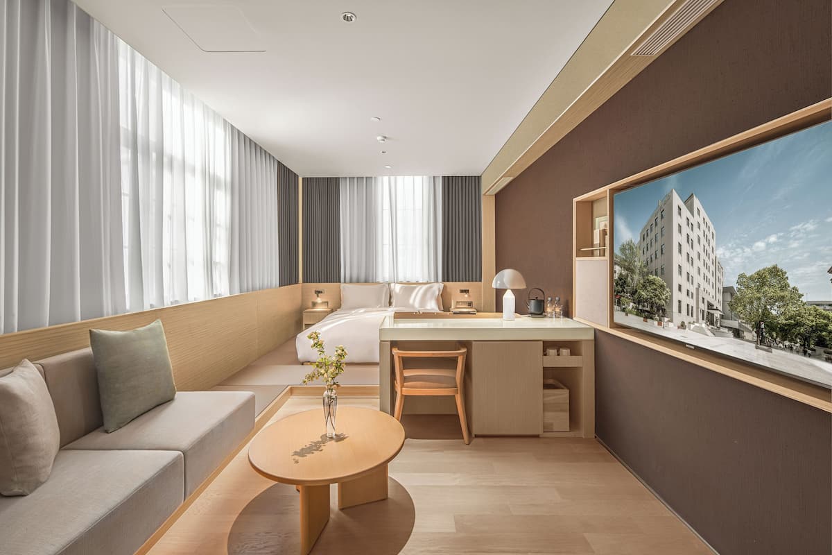Une chambre d’hôtel moderne équipée d’un lit, d’un bureau, d’un canapé et d’une grande fenêtre donnant sur la ville.
