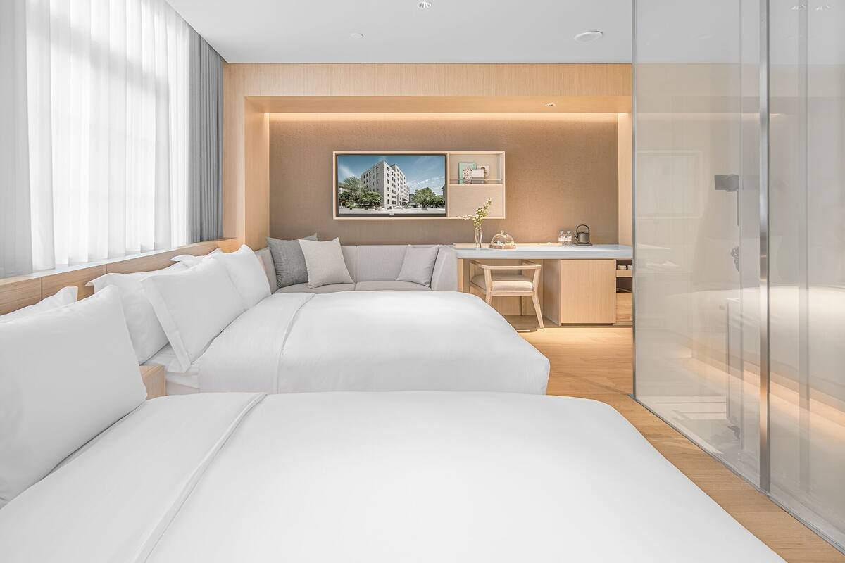 Une chambre d’hôtel moderne avec deux lits, un bureau et une vue sur le paysage urbain.