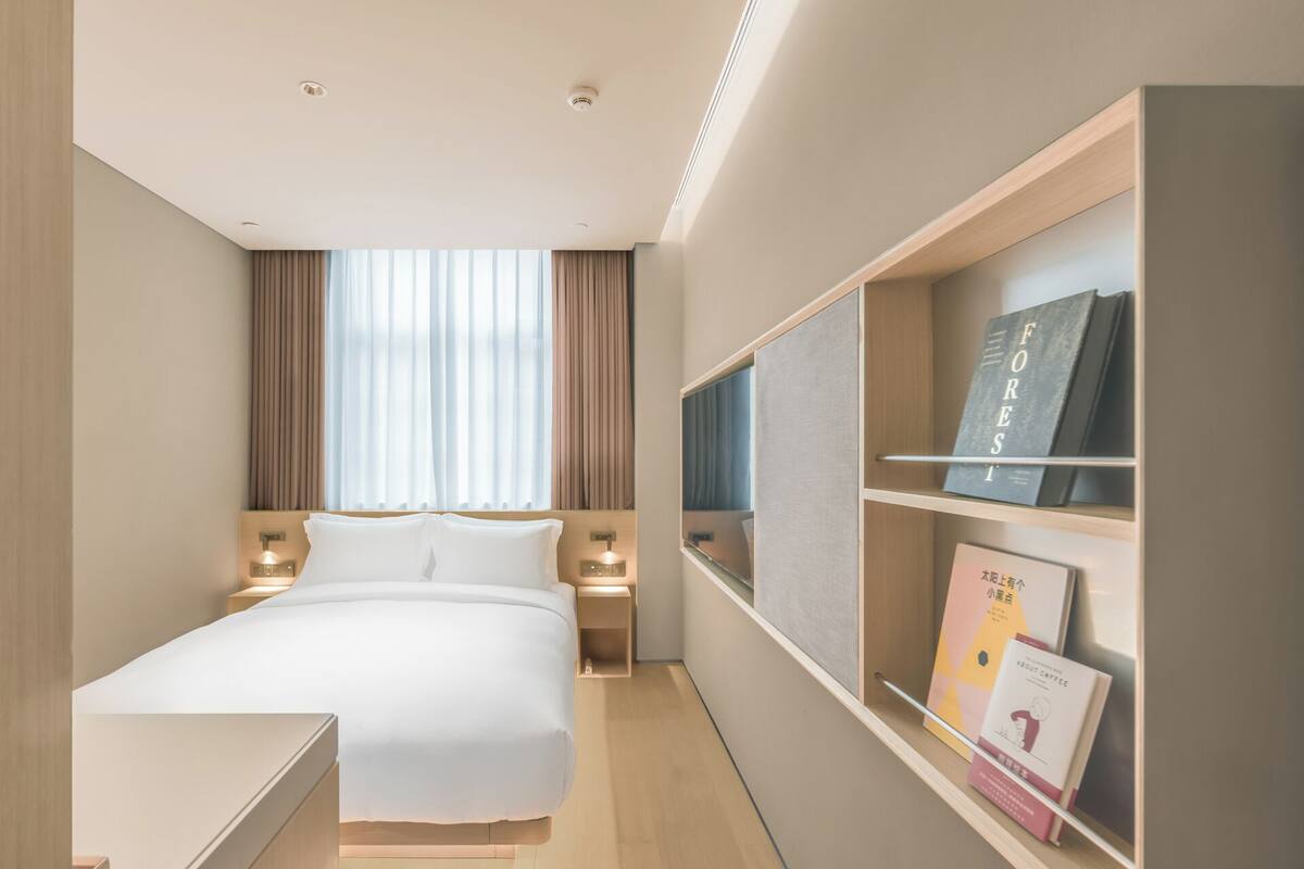 Une chambre d’hôtel moderne avec un grand lit, des lampes de chevet, un téléviseur intégré et une bibliothèque remplie de livres.