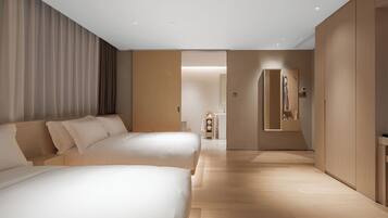 A modern hotel room with a large bed, a smaller bed, a wooden wardrobe, and a bathroom visible through an open door.