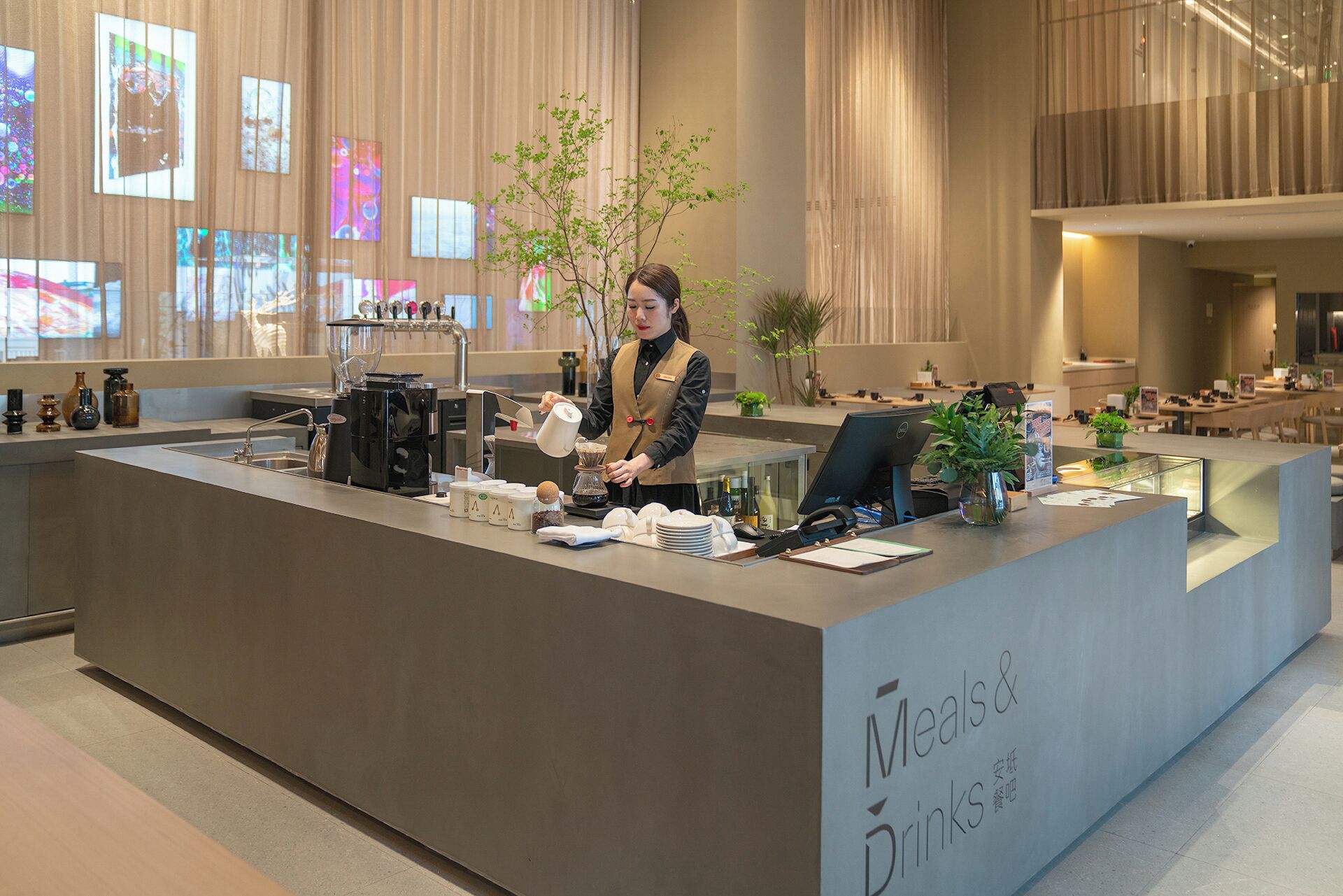 Un taulell de recepció modern amb una màquina de cafè, una planta i un panell informatiu.