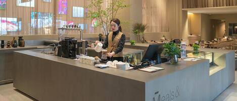 Un taulell de recepció modern amb una màquina de cafè, una planta i un panell informatiu.