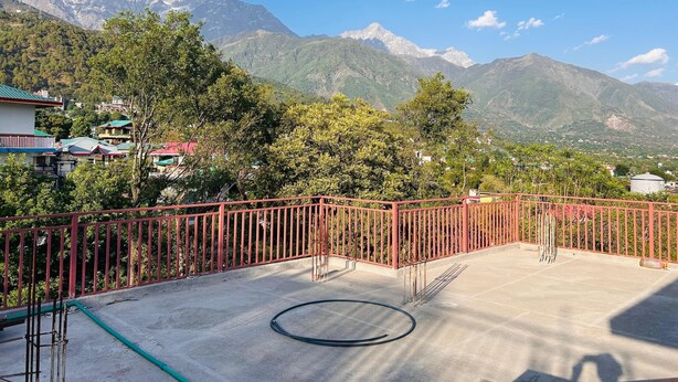 Une terrasse sur le toit offrant une vue sur des montagnes enneigées, avec une rambarde en métal rouge et un sol en béton.